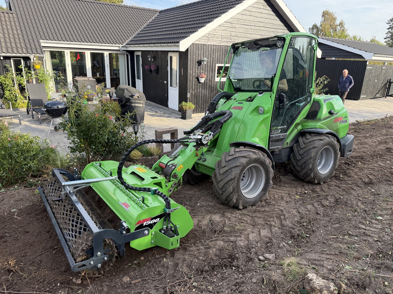 Grøn Avant med jordbearbejdningsredskab på det ryddede areal foran sommerhuset.