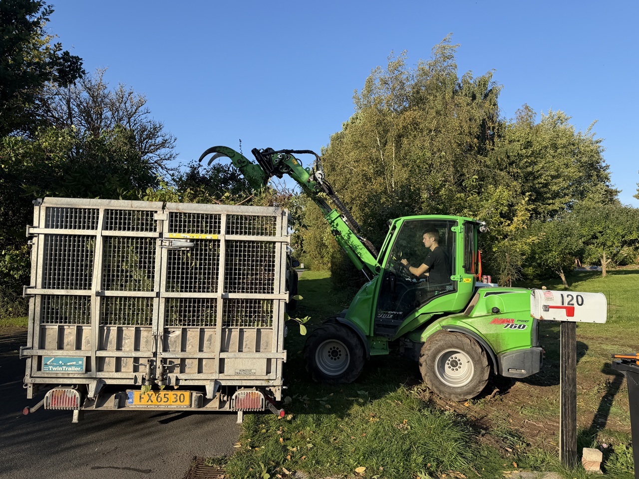 Grøn Avant læsser grene på en høj trailer ved indkørslen til sommerhuset.