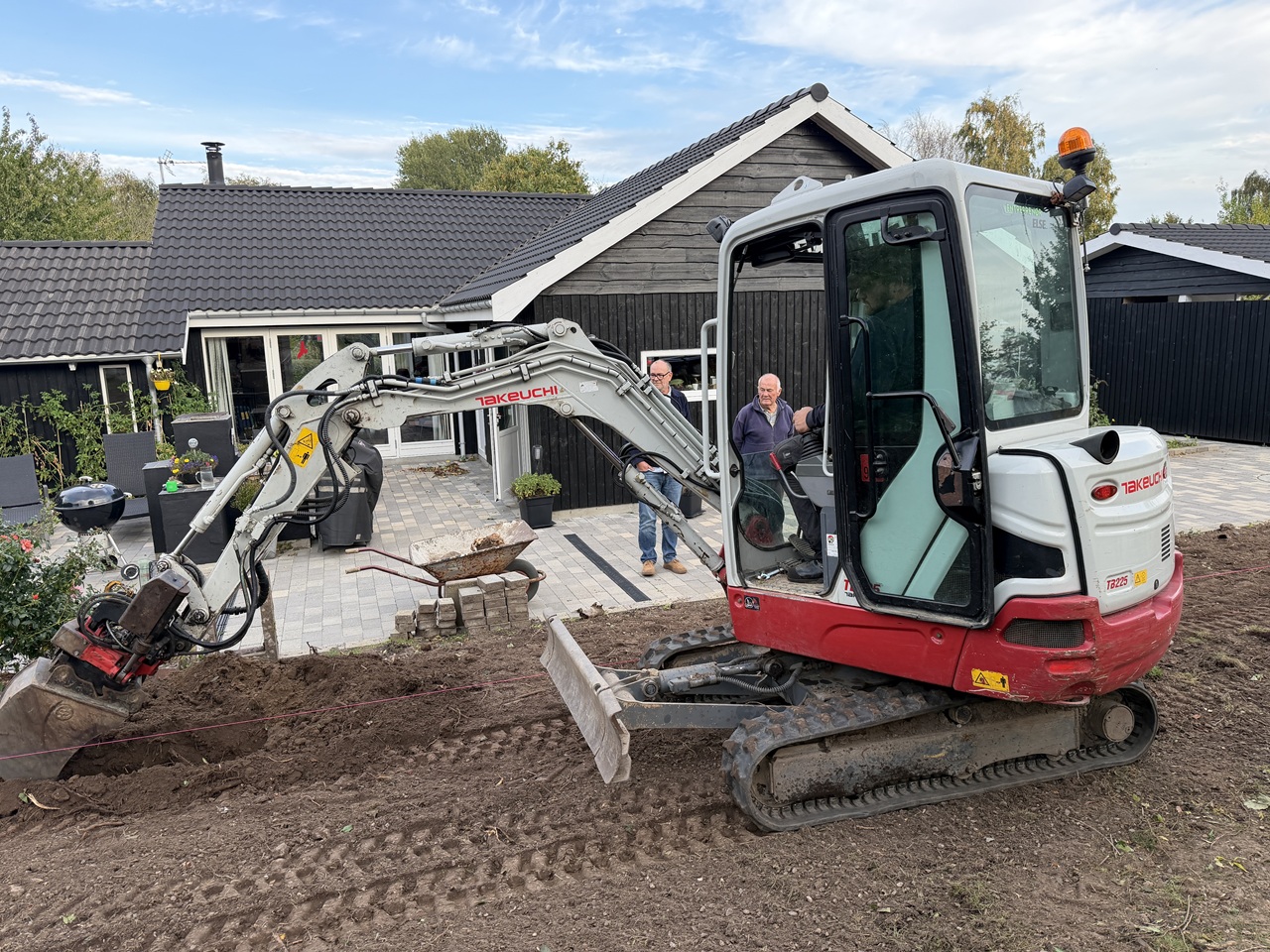 Minigraver med skovlen ved jorden langs det tidligere hækløb foran sommerhuset.